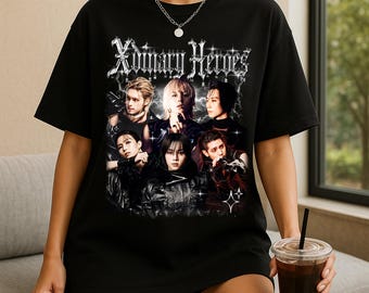 Könnte beinhalten: Schwarzes T-Shirt mit einer Grafik von sieben Personen und dem Text "Ordinary Heroes" in einer gotischen Schrift. Das Bild hat eine Vintage-Ästhetik. Das T-Shirt hat einen Rundhalsausschnitt und scheint aus Baumwolle zu sein.