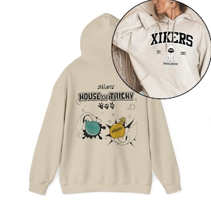 May include: A beige hoodie with a drawstring hood and long sleeves. The front features the text "xikers HOUSE OF TRICKY" with cartoon graphics of water balloons and a bomb. A circular inset shows the hoodie with "XIKERS" and a cartoon figure.