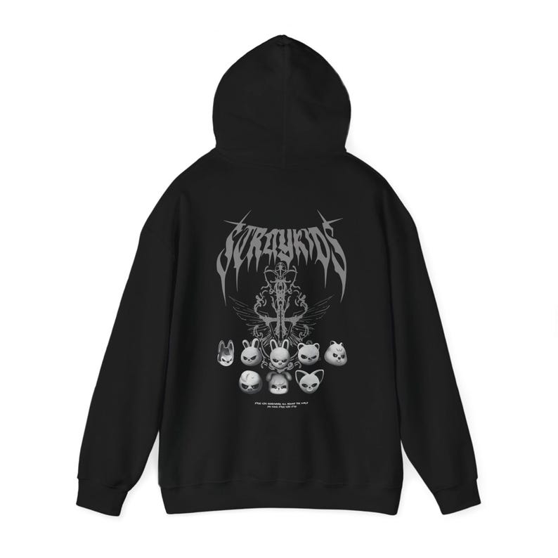 K&ouml;nnte beinhalten: Schwarzer Kapuzenpullover mit einem grafischen Design mit dem Text "Stray Kids" in einer stilisierten Schriftart. Das Design umfasst Cartoon-Tiergesichter und ein dekoratives Emblem. Der Kapuzenpullover hat eine Kapuze und lange &Auml;rmel.