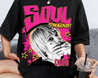 May include: Black t-shirt featuring a graphic design with the word "SOUL" in pink block letters above an image of a person with white hair. The design includes the text "PIHARMONY" and "DUH!" with yellow stars.