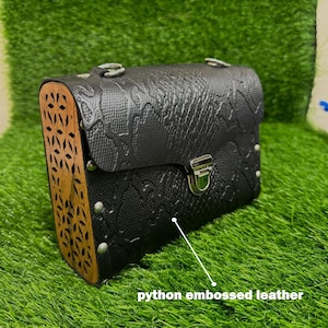 May include: Black python embossed leather handbag with a decorative wooden side panel. The bag features a silver-coloured clasp and hardware. The rectangular bag has a flap closure. The text 'python embossed leather' is visible.