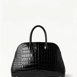 May include: A glossy black handbag with a crocodile skin texture. The bag has a rounded shape with a top handle and a zipper closure. The bag is set against a white background.