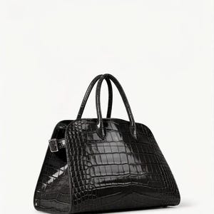 May include: A black, structured handbag with a crocodile-skin texture. The bag has two curved handles and a silver-tone buckle closure. The bag is a trapezoid shape and sits on a white background.