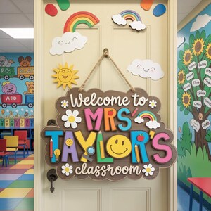 May include: A wooden classroom sign with the text "Welcome to MRS TAYLOR'S classroom" in colorful letters. The sign is decorated with daisies, rainbows, and a smiling face. The sign hangs on a cream-colored door.
