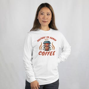 May include: White long-sleeve shirt with a cartoon coffee cup graphic and the text "Halfway to Human with Coffee".