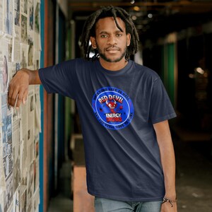 May include: Navy blue t-shirt with a circular graphic featuring a red devil and the text "RED DEVIL ENERGY DRINKS". The text "WHAT YOUR LIFE IS HELL BUT YOU STILL HAVE TO WORK" is also printed on the shirt.