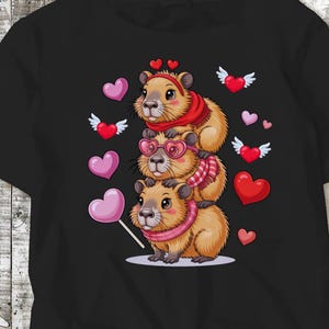 May include: Black t-shirt featuring a stack of three cartoon capybaras. The capybaras are wearing scarves, heart-shaped glasses, and headbands. Pink and red hearts and hearts with wings float around the capybaras. One capybara holds a heart-shaped lollipop.