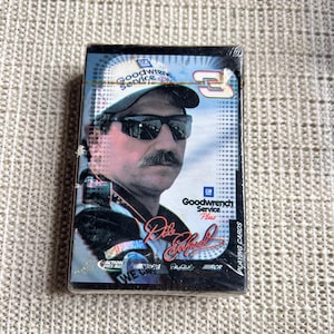 May include: Sealed deck of playing cards featuring a portrait of a man wearing sunglasses and a hat with the text "Goodwrench Service". The deck also includes the text "Dale Earnhardt" and "Playing Cards".