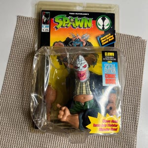 May include: A special edition Spawn comic book and Clown action figure in original packaging. The figure is a grotesque clown with a white head, red eyes, and a gaping mouth. The packaging includes the text "Clown Head turns into Violator Monster Head."