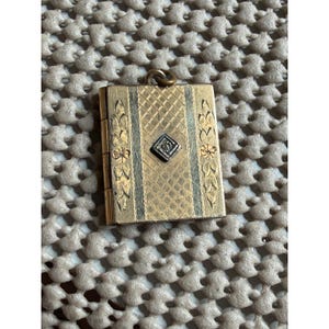 May include: A rectangular gold-tone metal locket featuring a central diamond-shaped silver-tone inlay. The surface is decorated with an etched cross-hatch pattern in the center, flanked by vertical panels with engraved floral and leaf motifs.