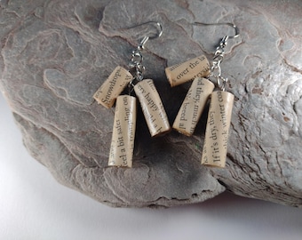 May include: A pair of earrings made from rolled up pages of a book. The earrings are silver and have a dangling design. The pages are printed with text, including the words "Snowdrops", "feel a bit safer", "very happy", "build a", "We breed al", "and they, much", "s over the la", "rrysic", "ks as", "If it's dry, they", "thick winter coa".