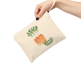 Könnte beinhalten: Cremefarbene Canvas-Tasche mit Reißverschluss und Handschlaufe. Sie zeigt eine Aquarell-Illustration von drei Karotten mit grünen Spitzen und dem Text "Farmer's Market" in grüner Schrift.