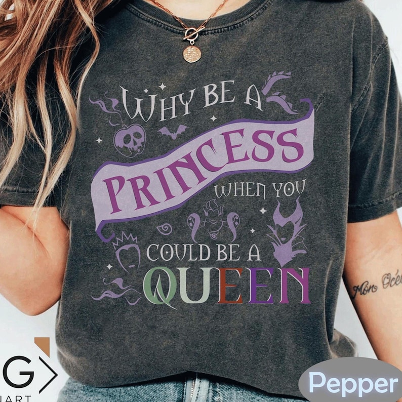 May include: Dark gray t-shirt with the text "Why be a Princess when you could be a Queen". The design includes a purple banner with the word "Princess", and the word "Queen" in multiple colors. The shirt has a vintage, distressed look.