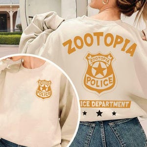 Pode incluir: Camisola creme com o texto "ZOOTOPIA" e um distintivo de pol&iacute;cia laranja. O distintivo inclui as palavras "ZOOTOPIA POLICE" e uma estrela. A camisola tamb&eacute;m tem as palavras "ICE DEPARTMENT" e tr&ecirc;s estrelas.