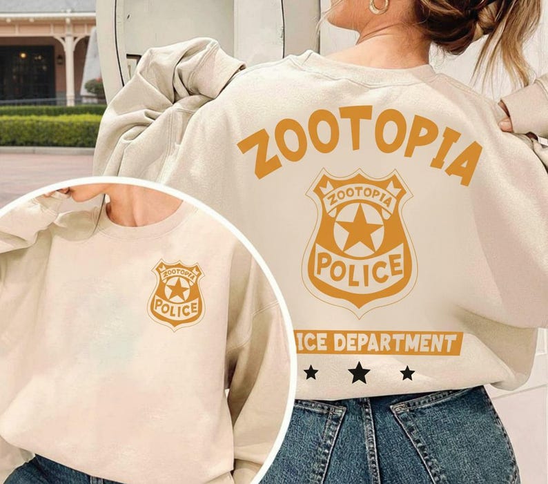 Pode incluir: Camisola creme com o texto "ZOOTOPIA" e um distintivo de pol&iacute;cia laranja. O distintivo inclui as palavras "ZOOTOPIA POLICE" e uma estrela. A camisola tamb&eacute;m tem as palavras "ICE DEPARTMENT" e tr&ecirc;s estrelas.