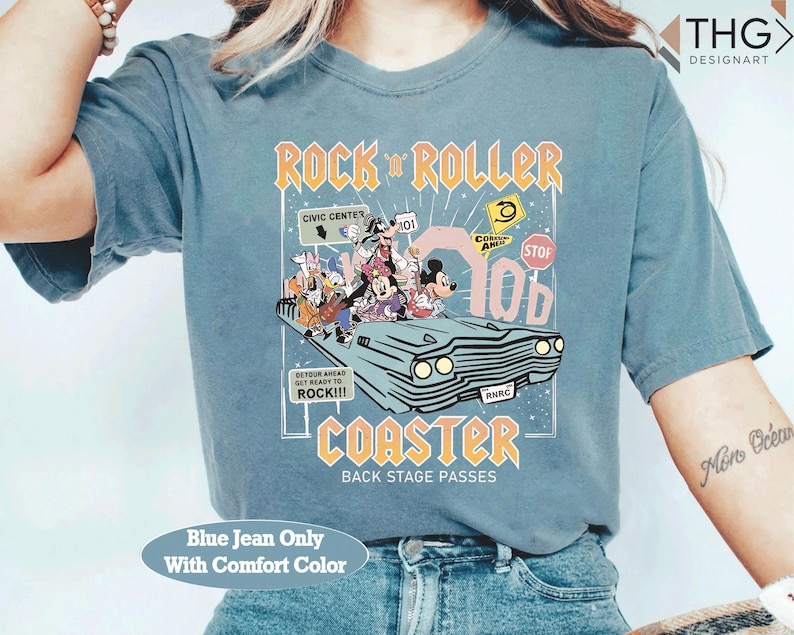 Puede incluir: Una camiseta azul vaquera con un gr&aacute;fico de personajes de Disney en un coche, con el texto "ROCK 'N ROLLER COASTER" en naranja y amarillo. La camiseta tambi&eacute;n tiene el texto "BACK STAGE PASSES" y "Blue Jean Only With Comfort Color".