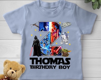 May include: A light blue short-sleeve t-shirt featuring a large number two graphic filled with Star Wars character imagery, including Darth Vader and R2-D2. Below the graphic, the text reads THOMAS BIRTHDAY BOY in bold black capital letters.