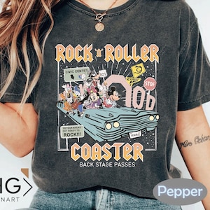Puede incluir: Camiseta gris oscuro con un gr&aacute;fico colorido de personajes de Disney en un coche retro, con las palabras "Rock 'n' Roller Coaster" y "Back Stage Passes". El dise&ntilde;o incluye se&ntilde;ales de tr&aacute;fico y el texto "Detour Ahead Get Ready to Rock!!!".