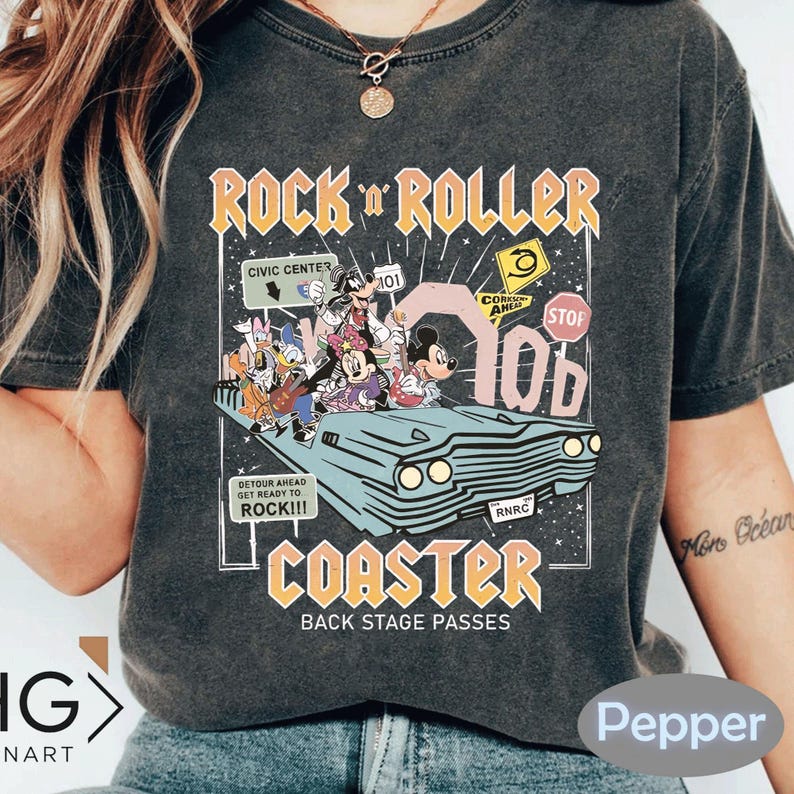 Puede incluir: Camiseta gris oscuro con un gr&aacute;fico colorido de personajes de Disney en un coche retro, con las palabras "Rock 'n' Roller Coaster" y "Back Stage Passes". El dise&ntilde;o incluye se&ntilde;ales de tr&aacute;fico y el texto "Detour Ahead Get Ready to Rock!!!".