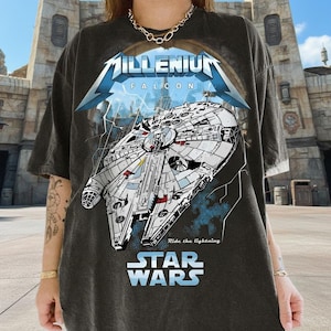 May include: Dark gray t-shirt featuring a graphic of the Millennium Falcon spaceship with the text "Millennium Falcon" and "Star Wars". The design includes a blue lightning bolt and the phrase "Ride the lightning".