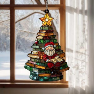 May include: A stained glass suncatcher shaped like a Christmas tree constructed from stacked books. A figure of Santa Claus sits in the center reading an open book. The tree is topped with a yellow star and features green, brown, and red tones.