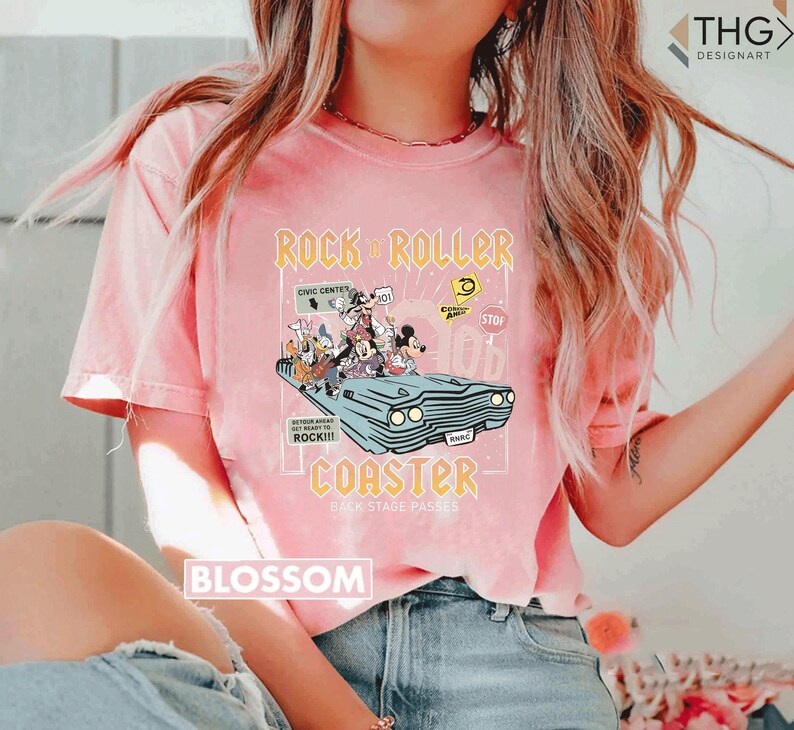 Puede incluir: Camiseta rosa claro con un gr&aacute;fico de personajes de Disney en un coche azul claro, con las palabras "Rock 'n' Roller Coaster" y "Back Stage Passes". La camiseta tambi&eacute;n tiene la palabra "Blossom" impresa.