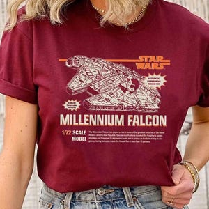 Puede incluir: Camiseta burdeos con una ilustración detallada del Halcón Milenario de Star Wars. El diseño incluye el texto "STAR WARS" y "MILLENNIUM FALCON" con texto adicional sobre el modelo.