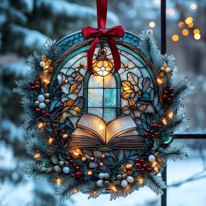 May include: A circular stained glass ornament featuring an open book and a lantern design, illuminated by warm internal lights. The piece is framed by artificial pine branches, red berries, and white beads, topped with a red ribbon bow for hanging.