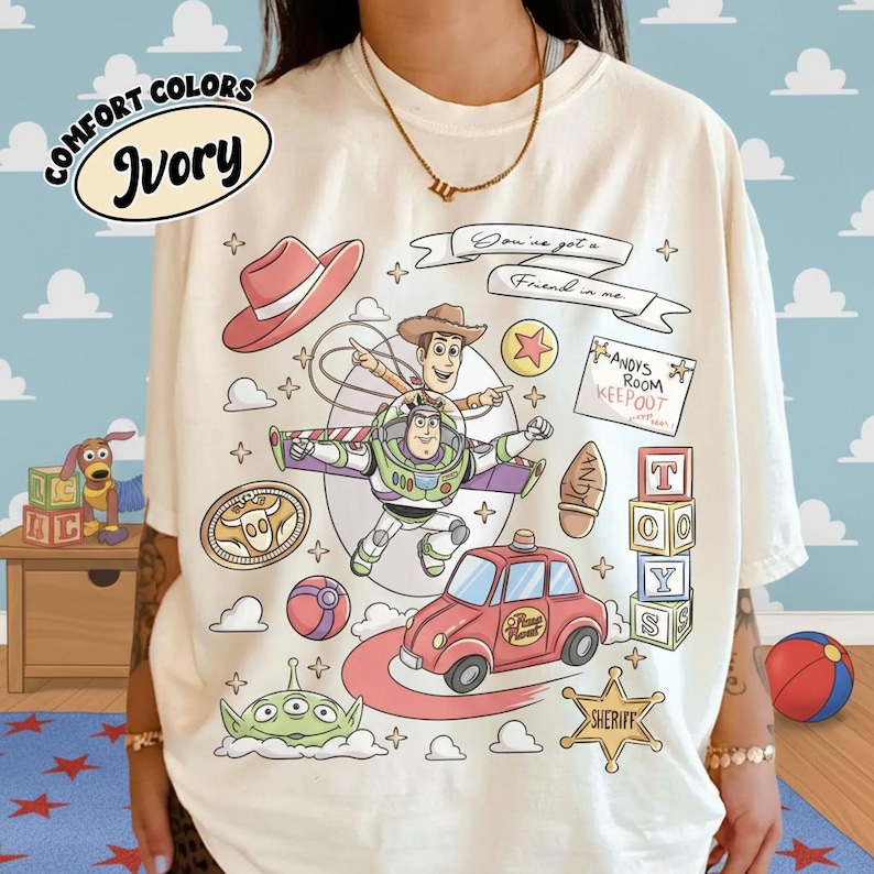 Op de afbeelding: Ivoor kleurig T-shirt met een kleurrijke afbeelding van tekenfilmfiguren. Het ontwerp bevat Woody, Buzz Lightyear, een rode auto en de tekst "You've got a Friend in me."