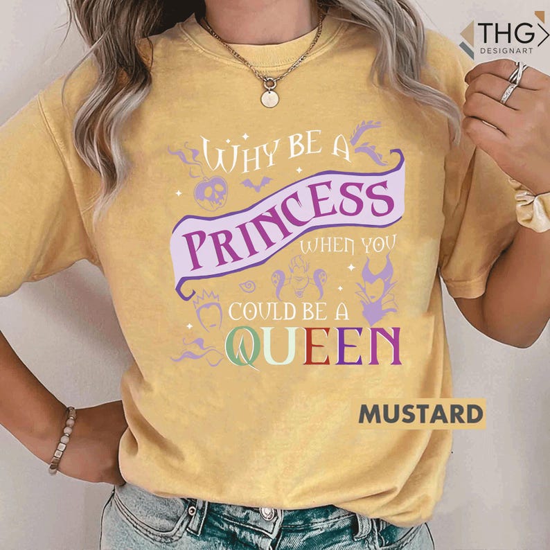 May include: Mustard-colored t-shirt with the text "Why be a Princess when you could be a Queen" in purple and green. The design includes a skull, bats, and other graphics. The word "Mustard" is printed at the bottom.