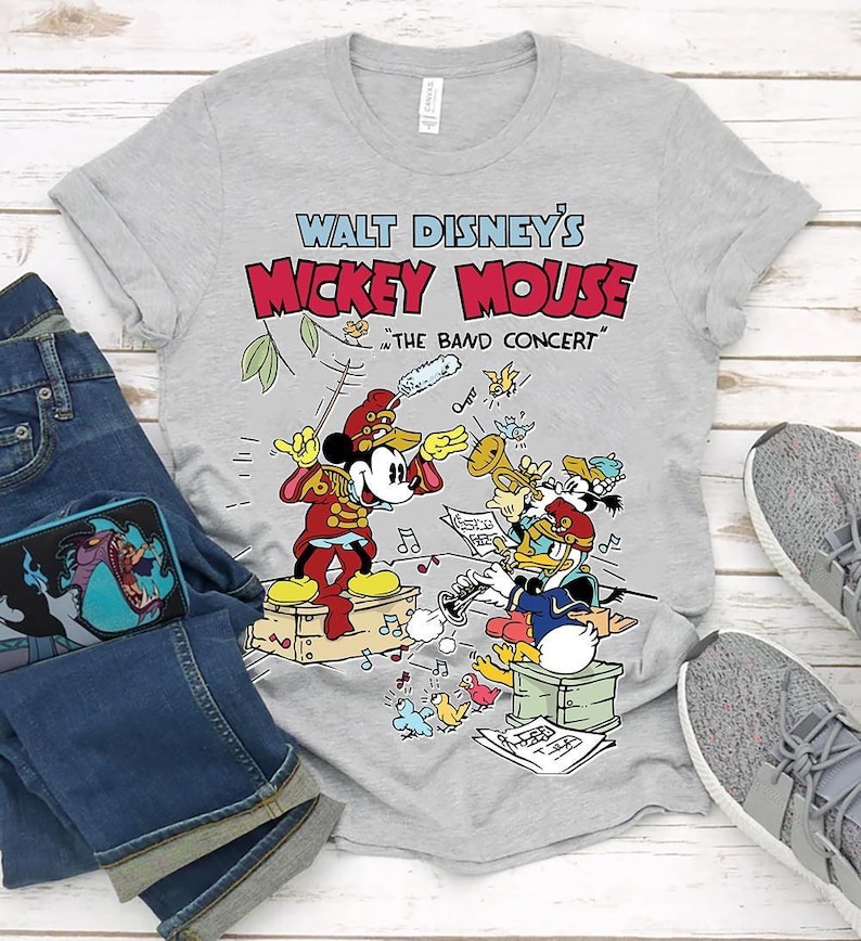 May include: A gray t-shirt featuring a colorful graphic of Mickey Mouse conducting a band, with Donald Duck playing a trumpet. The text "Walt Disney's Mickey Mouse" is above the image, with "The Band Concert" below.
