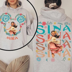 May include: A light grey hoodie with a cartoon character in a pink and cream dress. The front features the name "MIRA" and a heart-shaped floral design. The back of the hoodie displays the name "SINA" in colourful letters.