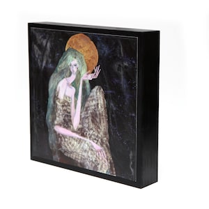 May include: A framed painting of a woman with long green hair sitting in a flowing gown. She is looking to the right, and a large golden circle is behind her head. The background is dark blue with white and gold accents.