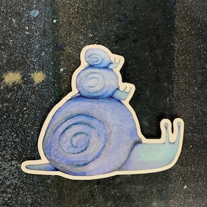 May include: A watercolor painting of three blue snails stacked on top of each other. The snails are painted in shades of blue and purple, with a white outline.