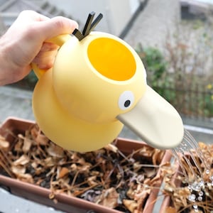May include: A yellow duck-shaped watering can with a black handle and a white spout is being used to water a potted plant. The plant is in a brown pot and has brown leaves.