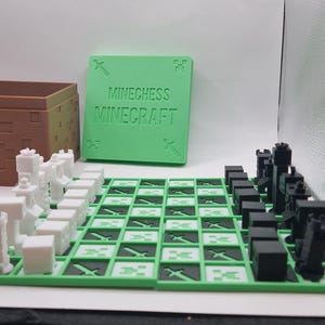 Op de afbeelding: Een Minecraft-thema schaakspel met een groen en zwart geblokt bord. De stukken zijn zwart en wit, en een groene doos met de woorden "Minechess Minecraft" staat op de achtergrond. Een bruine doos is ook zichtbaar.