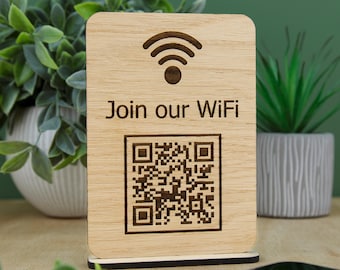 May include: A rectangular light-colored wooden sign with rounded corners, featuring a dark brown laser-engraved Wi-Fi symbol, the text "Join our WiFi," and a square QR code. The sign is mounted on a thin, dark brown rectangular base.