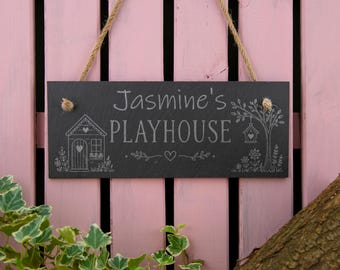 May include: A rectangular black slate sign hanging by a jute rope. The sign features the engraved text "Jasmine's PLAYHOUSE" in the center, flanked by an illustration of a small house on the left and a tree with a birdhouse on the right.