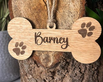 May include: Wooden dog bone ornament with the name "Barney" engraved on it. The ornament has two paw prints on either side of the name.