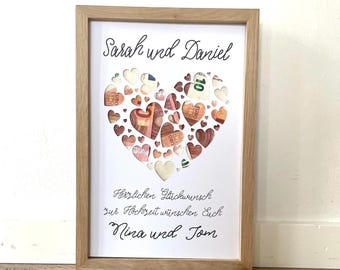 May include: A white frame with a wooden border contains a heart-shaped design made of paper cutouts. The cutouts are filled with euro bills. The text "Sarah und Daniel" is at the top of the frame, and the text "Herzlichen Glückwunsch zur Hochzeit wünschen Euch Nina und Tom" is at the bottom.