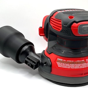 May include: A red and black Craftsman random orbit sander with a black dust collection port. The sander has a power button and warning labels. The tool is designed for sanding and surface preparation.