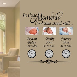 May include: A beige wall with a black vinyl decal that reads "In these Moments time stood still..." with three black and white clock faces and three framed photos of babies with their names and birth dates below each photo.