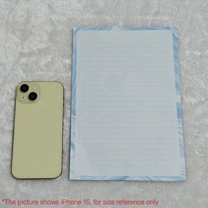 May include: A white lined notepad with a blue and white marbled design border. The notepad is next to a light green iPhone 15 for size reference.