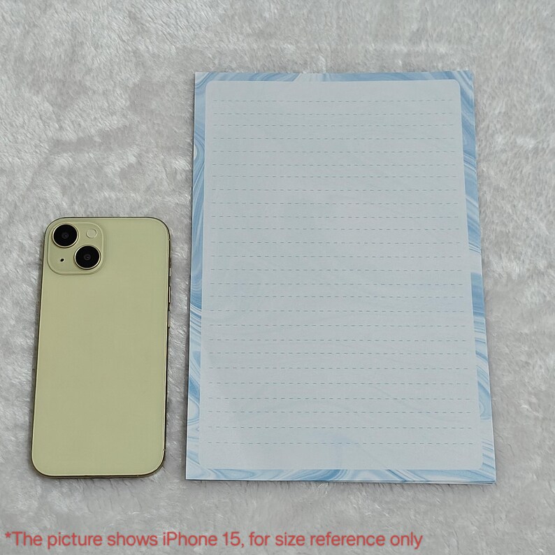 May include: A white lined notepad with a blue and white marbled design border. The notepad is next to a light green iPhone 15 for size reference.