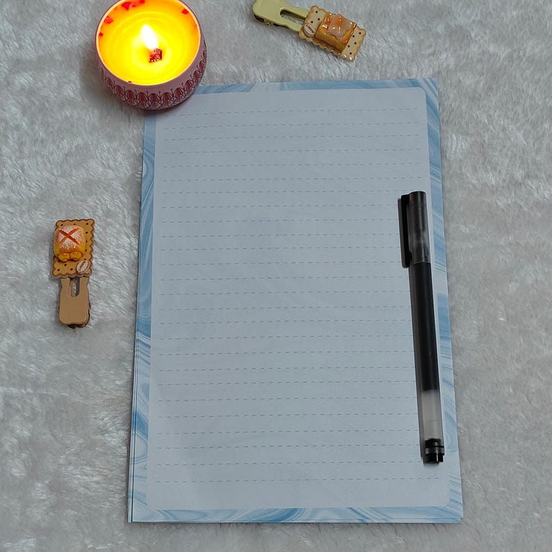 May include: A white lined notebook with a blue and white marbled design on the cover. A black pen is lying on the notebook.