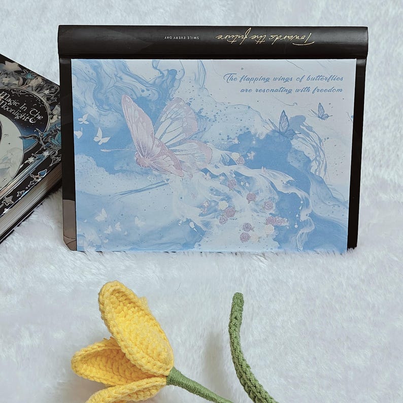 May include: A black journal with a blue and white marbled design and the text "The flapping wings of butterflies are resonating with freedom." The journal is closed and sitting on a white surface.