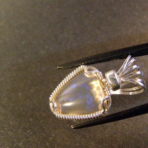 May include: A silver pendant featuring a delicate wire-wrapped opal gemstone. The pendant has an ornate bail with a delicate, intricate design.
