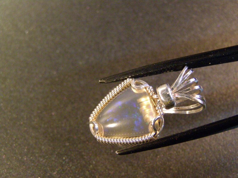 May include: A silver pendant featuring a delicate wire-wrapped opal gemstone. The pendant has an ornate bail with a delicate, intricate design.