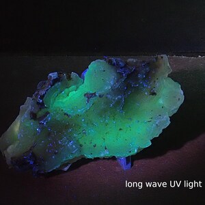 May include: A mineral specimen with a vibrant green and blue glow under long wave UV light. The rock has an irregular shape and a textured surface. The text "long wave UV light" is visible at the bottom of the image.