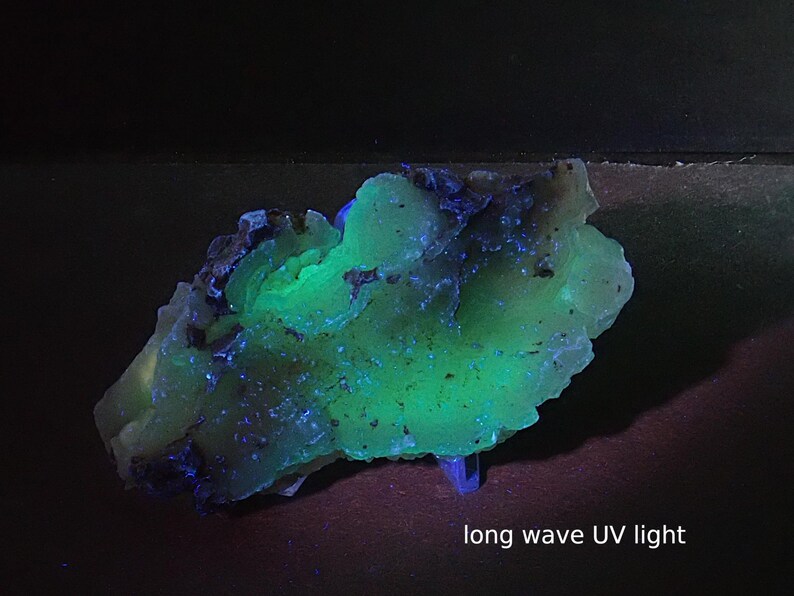 May include: A mineral specimen with a vibrant green and blue glow under long wave UV light. The rock has an irregular shape and a textured surface. The text "long wave UV light" is visible at the bottom of the image.